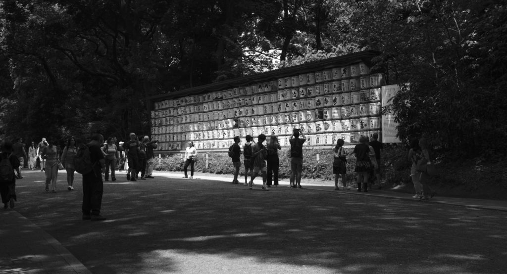 Black and white photo. A group of five people silhouetted against bright white sake barrels in the grounds of Meiji Jingu shrine.